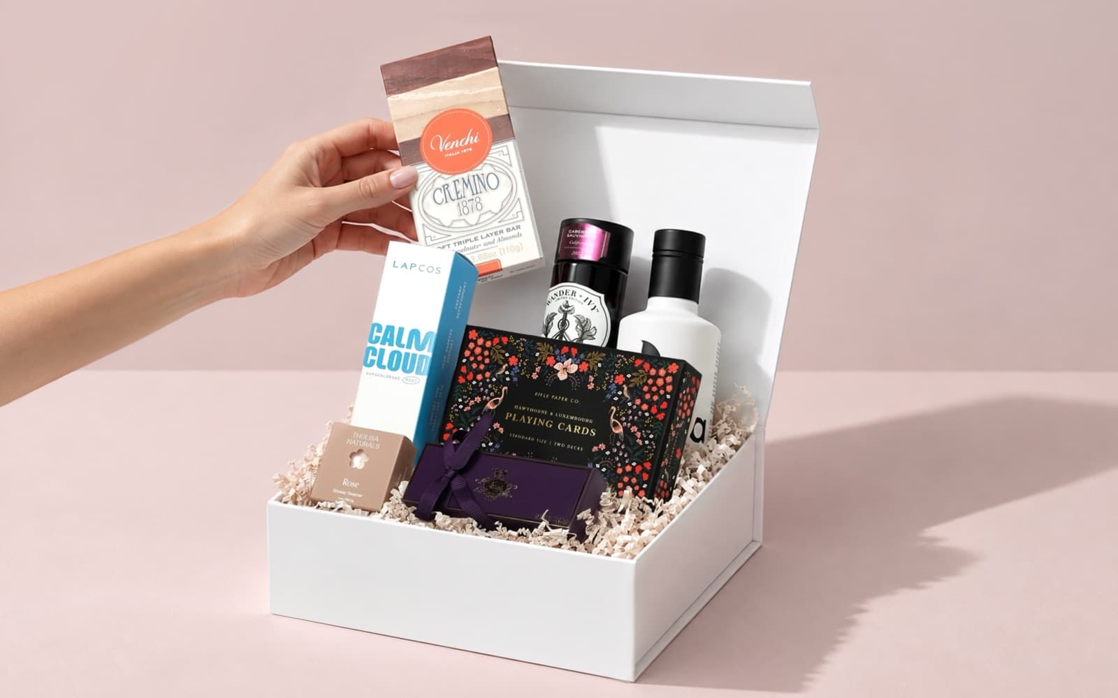 A hand adding a chocolate bar to an open white gift box